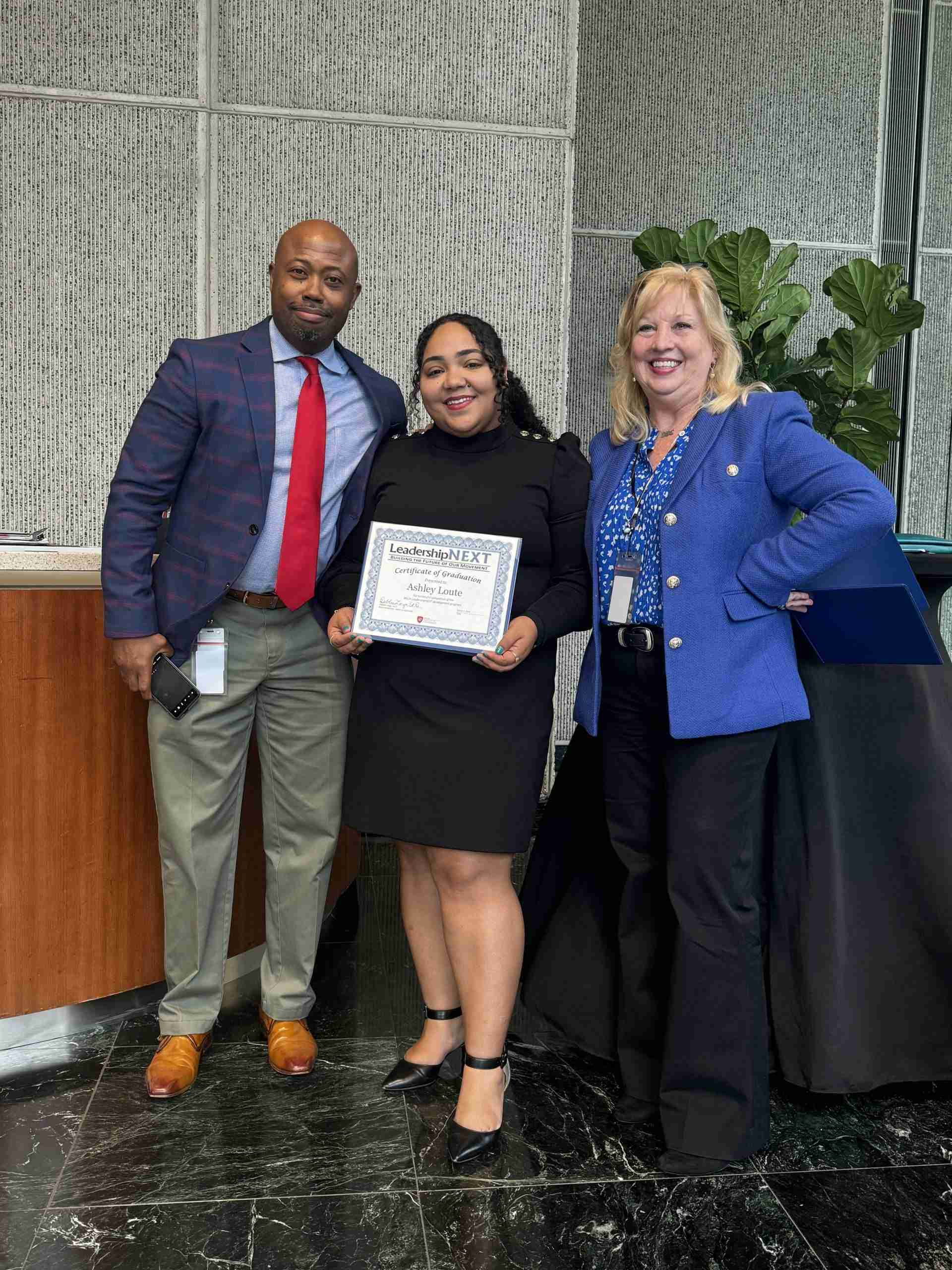 A Loute Leadership Picture of three people, person in center is BGC Polk Director of Finance and Administration Ashley Loute holding a certification of graduation from the Leadership Next Program.